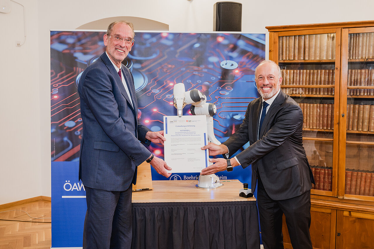 A robot passes the founding document from Heinz Faßmann, President of the Austrian Academy of Sciences, to Christoph Boehringer, Chairman of the Board of the Boehringer Ingelheim Foundation.